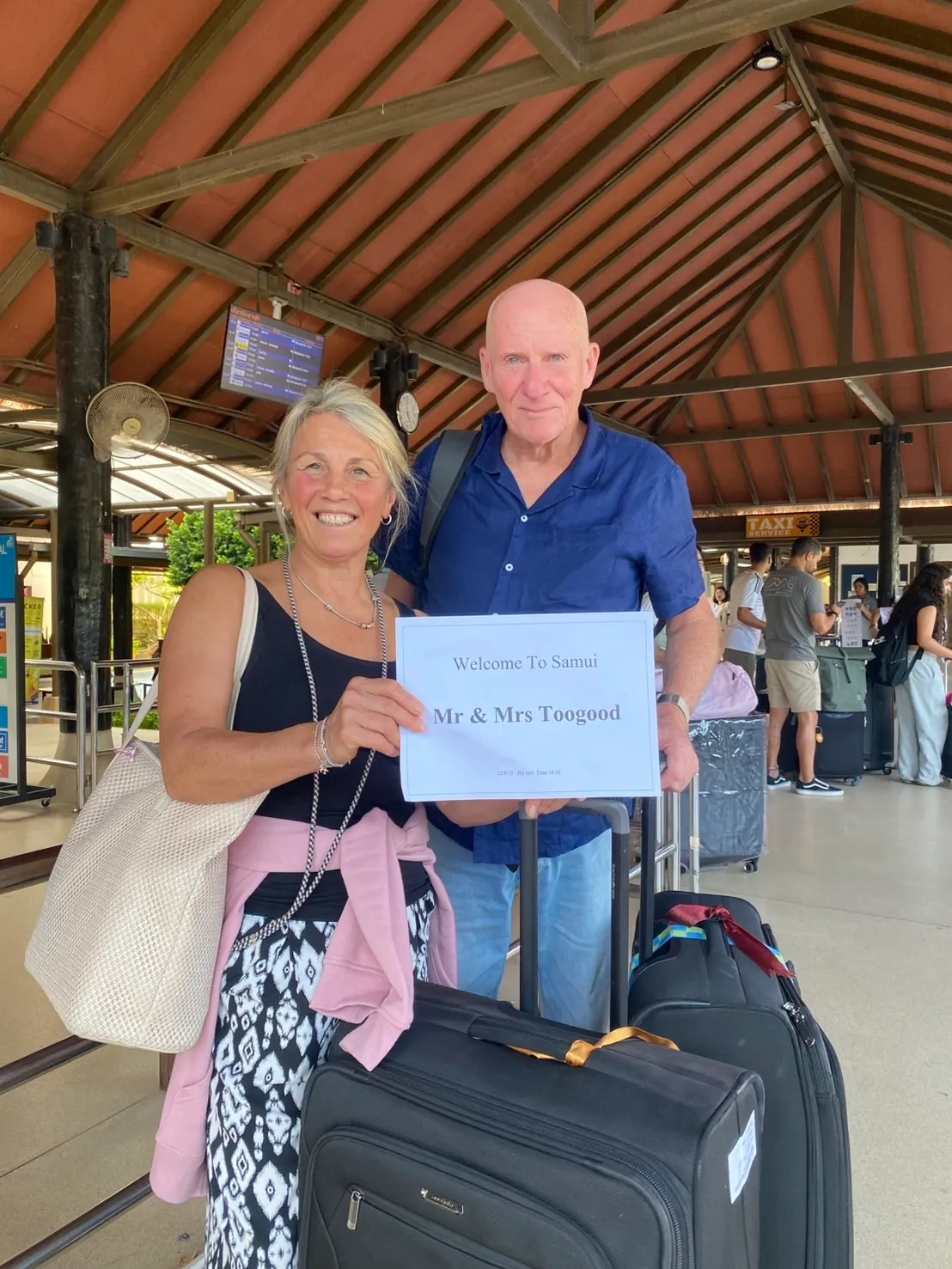 ลูกค้าคู่หนึ่งถือป้ายต้อนรับของ KB Samui ที่อาคารผู้โดยสารสนามบินสมุย